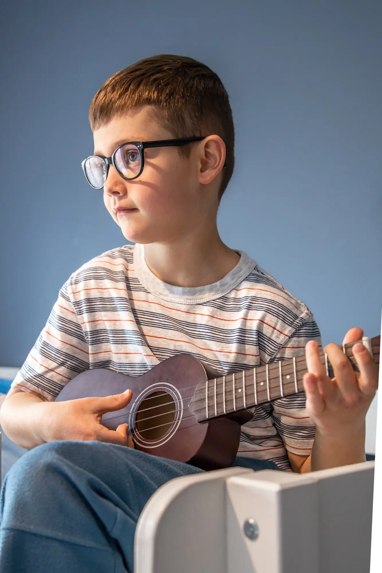 In seinem Zimmer zu Hause lernt ein süßer Junge mit Brille, die Ukulele-Gitarre zu spielen.